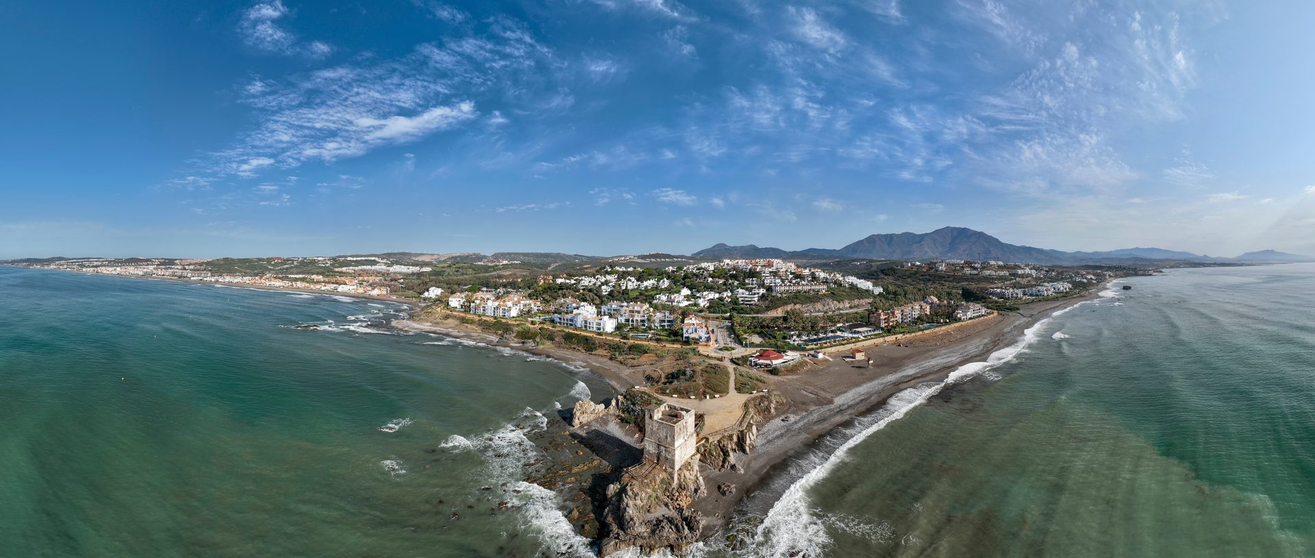 Aerial view of a coastal town with a beach, mountains, and a lighthouse.